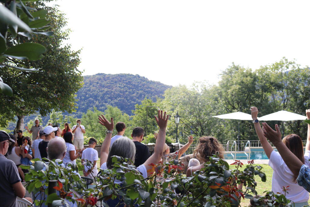 Gruppo di persone con braccia alzate in un'area all'aperto con piscina e natura.