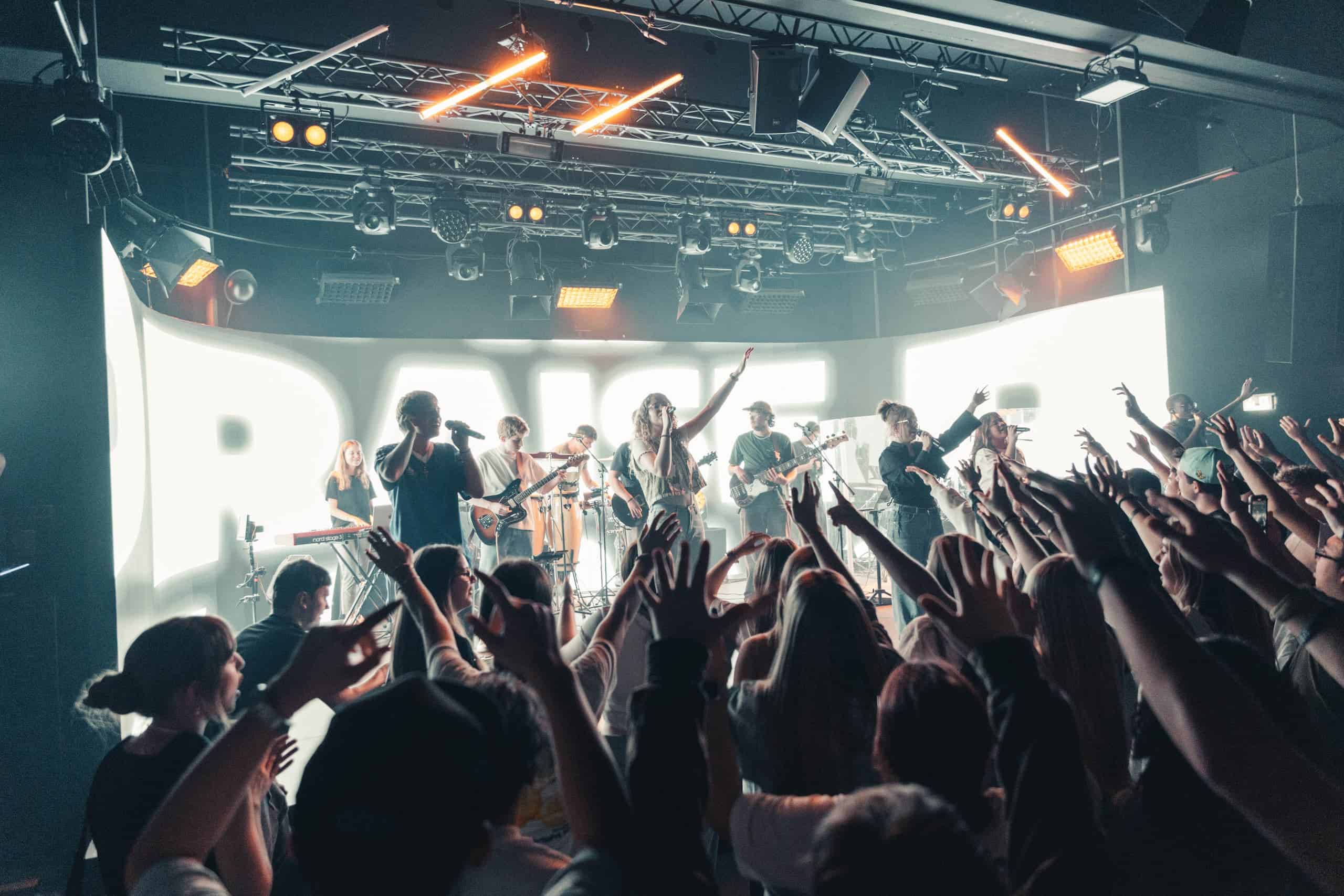 Bright stage with live music, exuberant crowd at a large church service event, youthful audience, modern church atmosphere, musical event, religious event in a church, inspiring community, gospel concert, community in Christ, dynamic live worship.