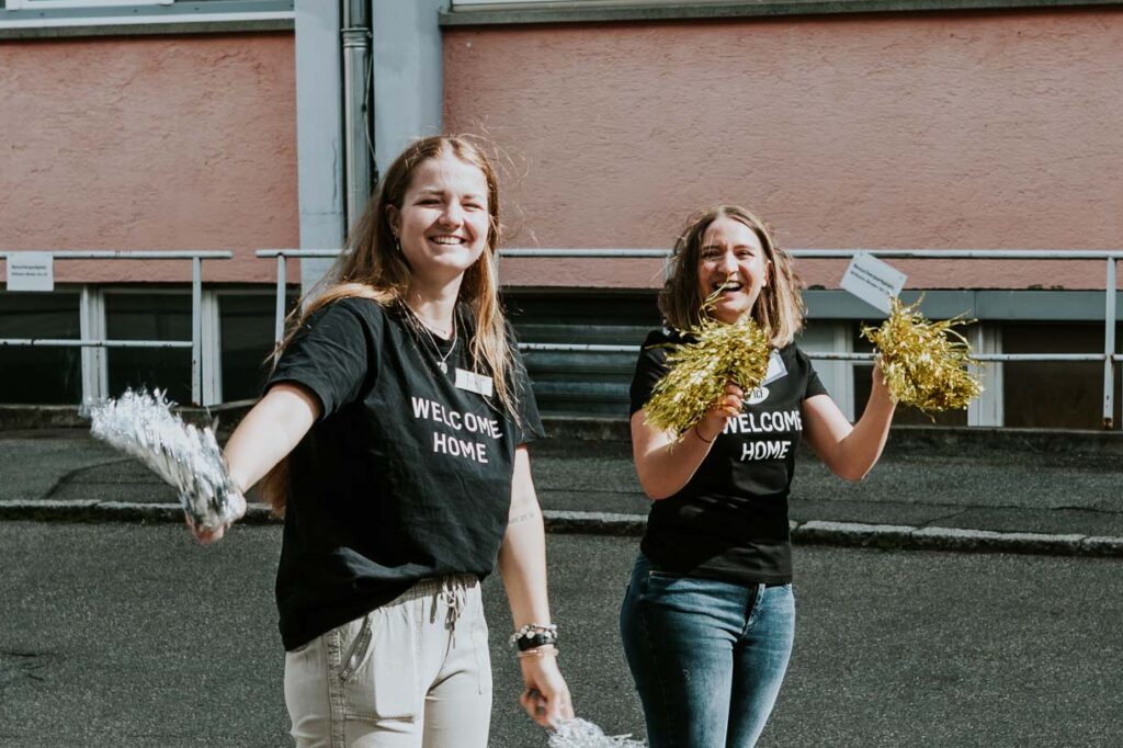 Zwei Frauen halten Pompons und lächeln in der Außenaufnahme.