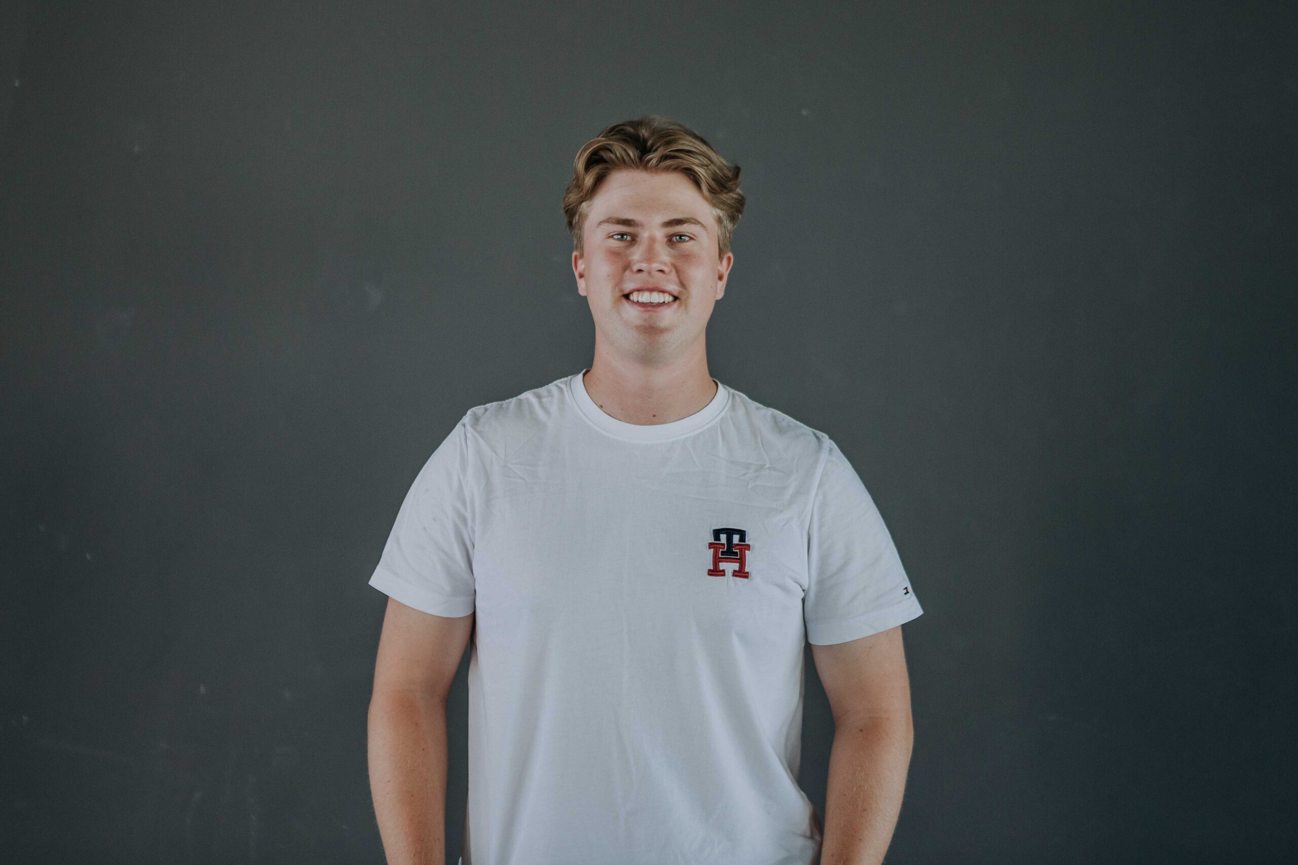 Junge Person in weißem T-Shirt vor grauem Hintergrund.