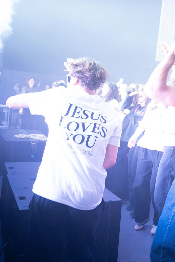 Person trägt T-Shirt mit "Jesus Loves You" auf einer Party.