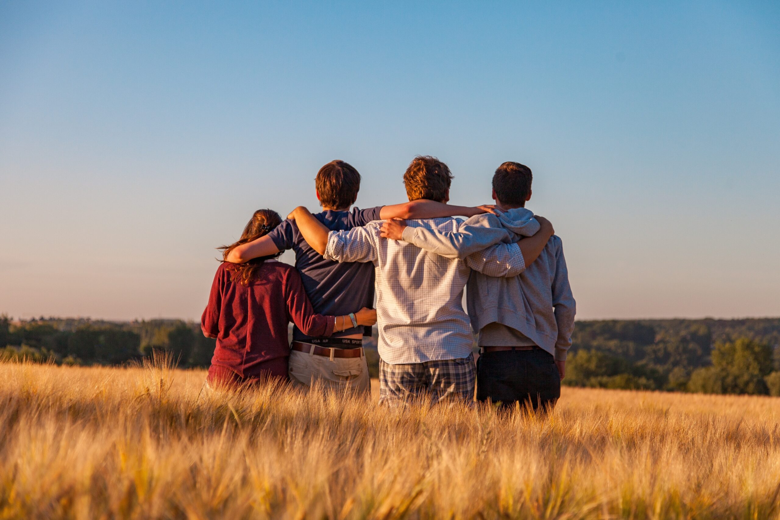 Vier Freunde stehen im Feld, mit Armen um die Schultern, Blick in den Himmel.