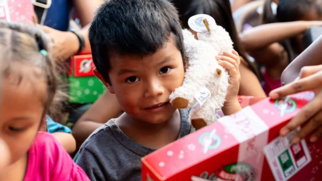 Junge boy mit Plüschtier in der Hand, umgeben von anderen Kindern und Geschenken.