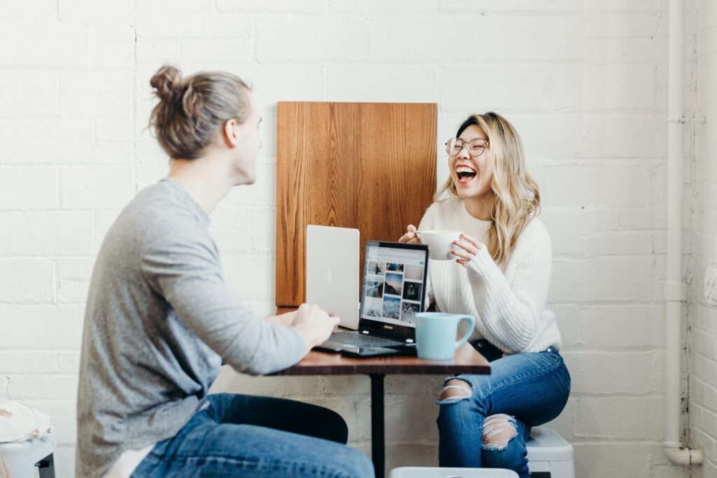 Zwei Frauen im Gespräch bei einem Online-Meeting, sitzen an einem Tisch mit Laptop und Tasse, in einem hellen Raum.