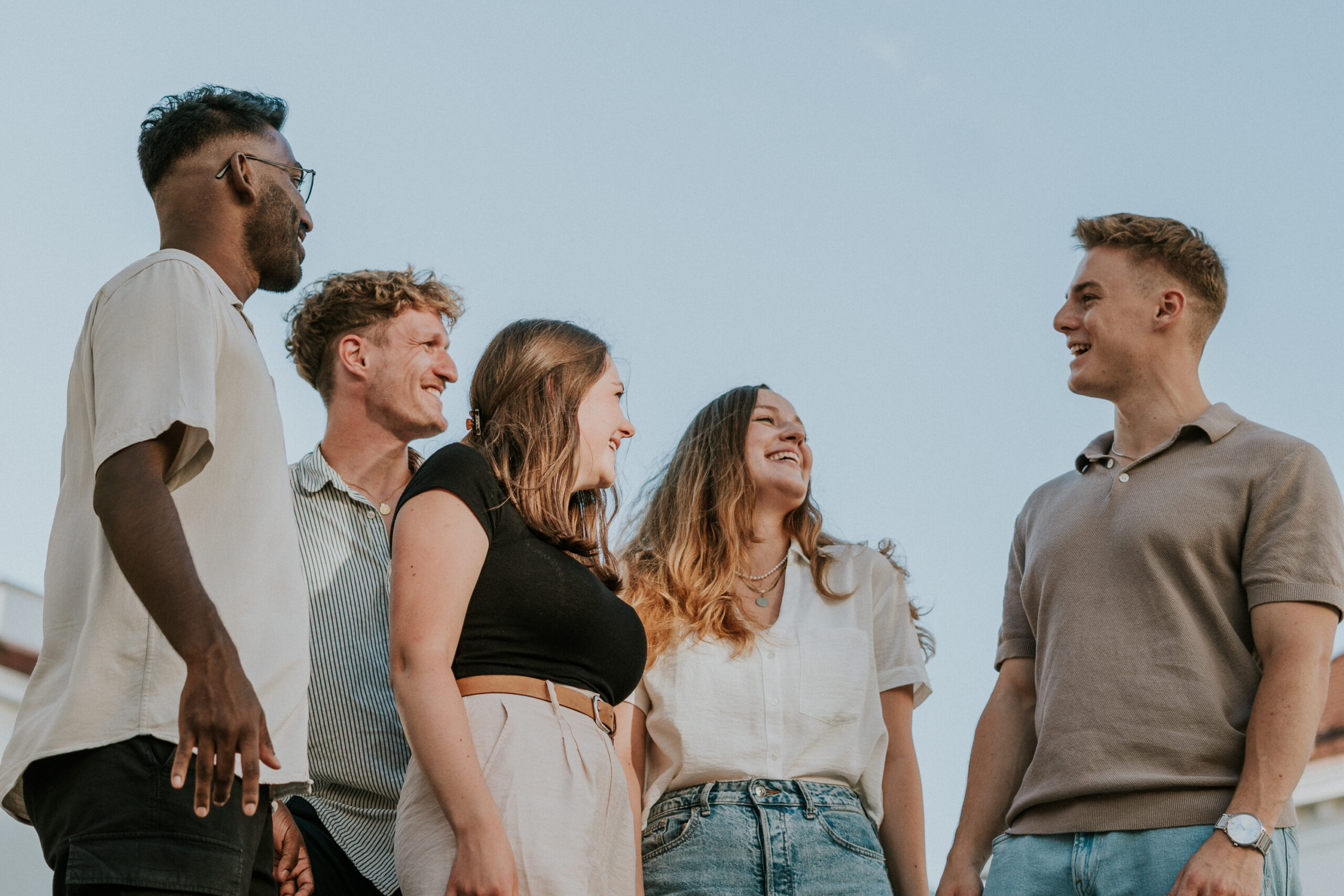 Sechs junge Menschen stehen im Freien, lachen und sprechen miteinander.