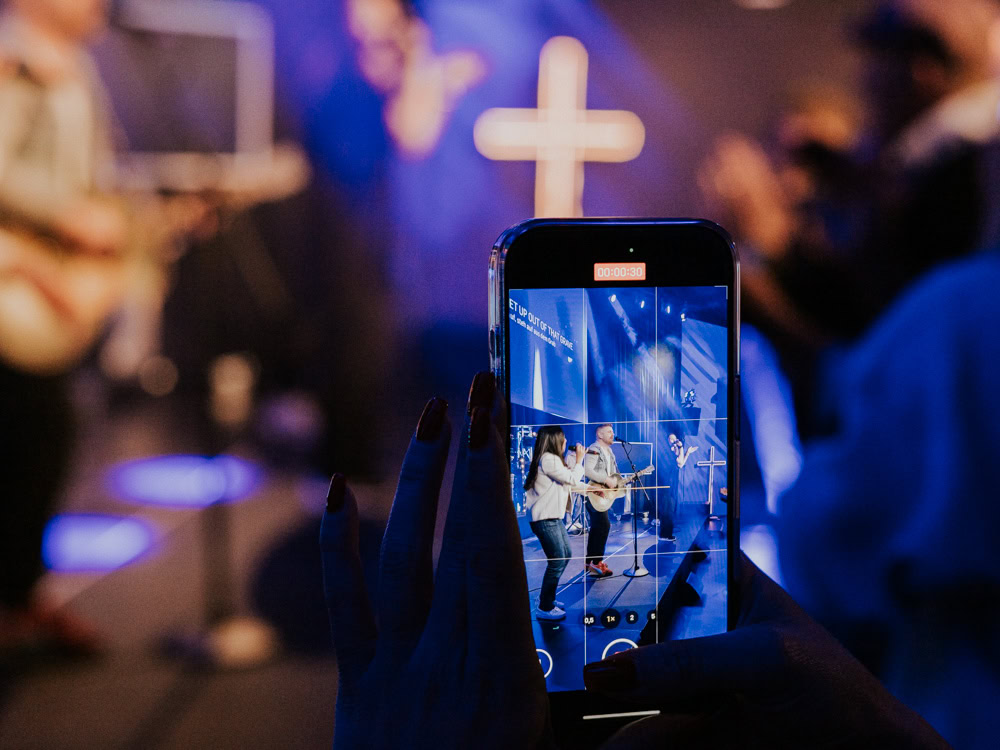 Personen auf der Bühne spielen Gitarre, während eine Person im Vordergrund ein Smartphone zur Aufnah.