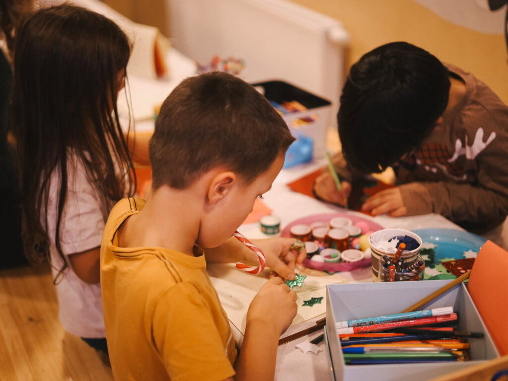 Kinder beim Basteln mit Farben und Dekorationen auf einem Tisch.