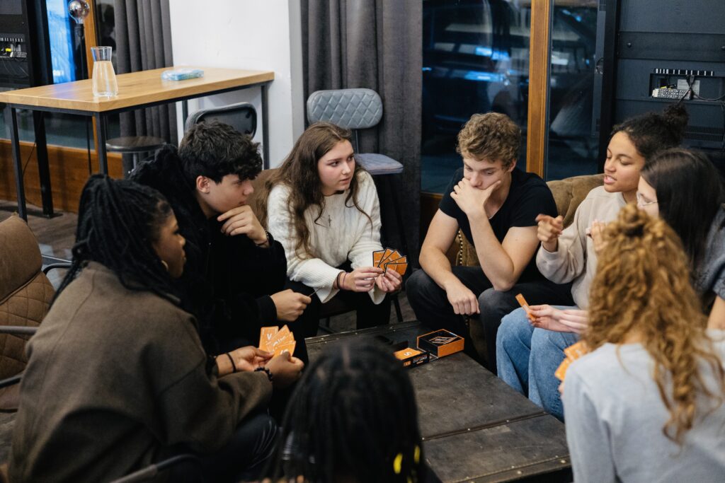 Jugendliche sitzen um einen Tisch, spielen ein Kartenspiel.
