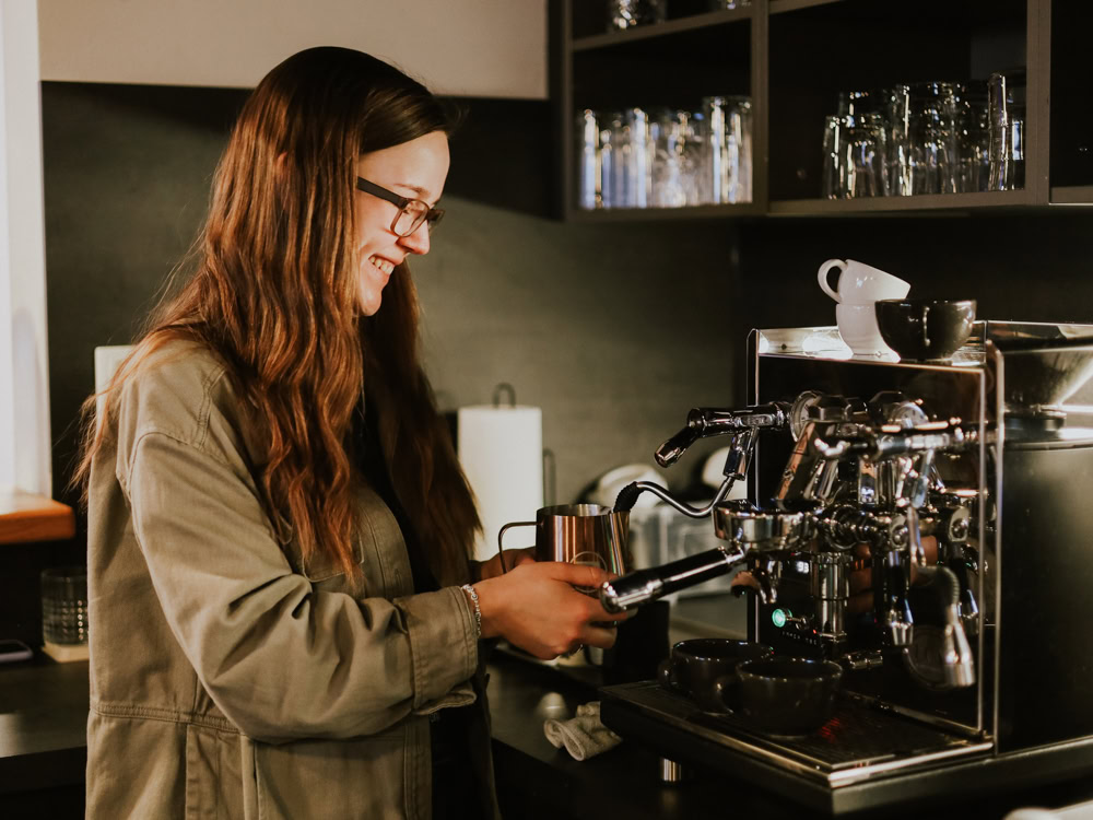 Eine Frau mit Brille bereitet einen Espresso in einer Kaffeebar zu.
