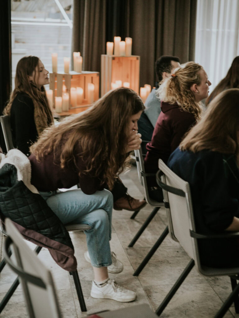 Gruppe von Menschen sitzt in einem Raum mit Kerzen und Vorhängen.