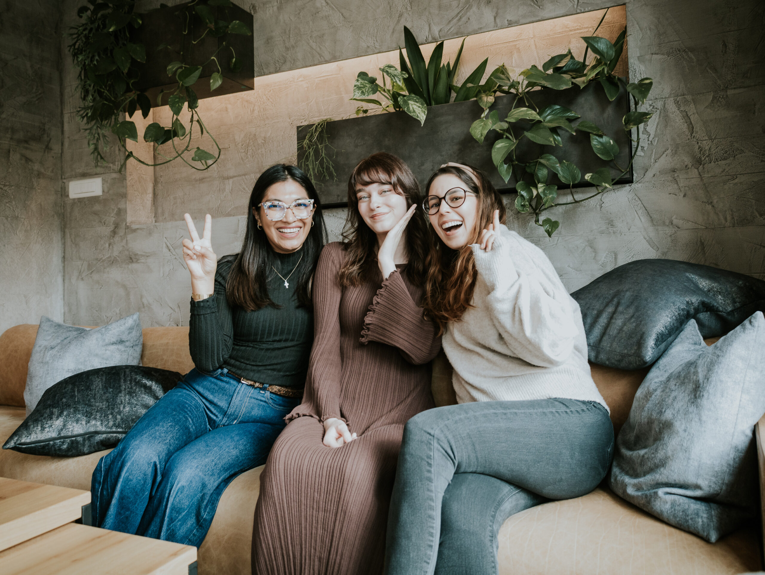 Drei Frauen sitzen auf einer Couch, lachen und machen Peace-Zeichen.
