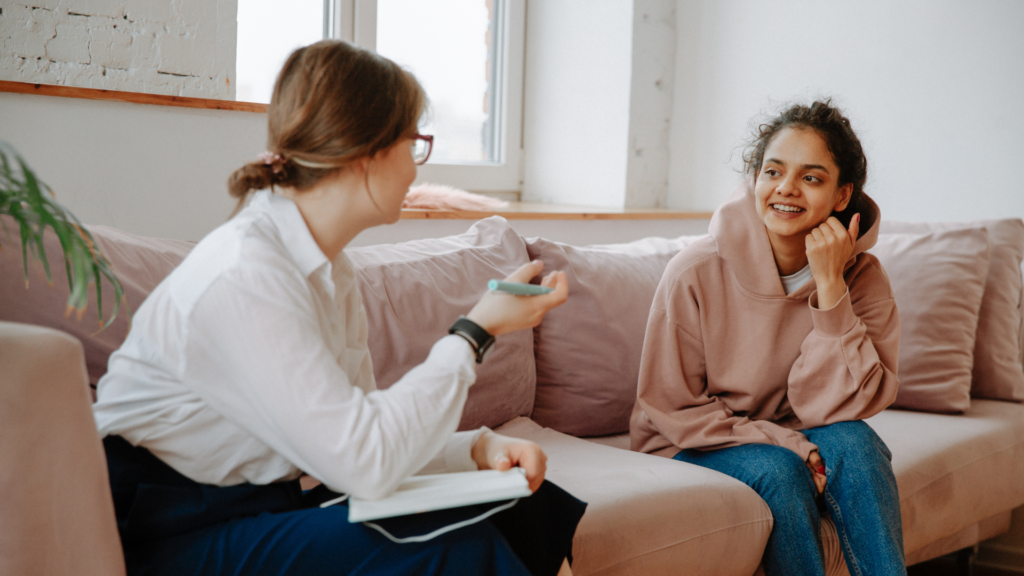 Zwei Frauen sitzen auf einem Sofa, eine spricht am Telefon, die andere hört zu.
