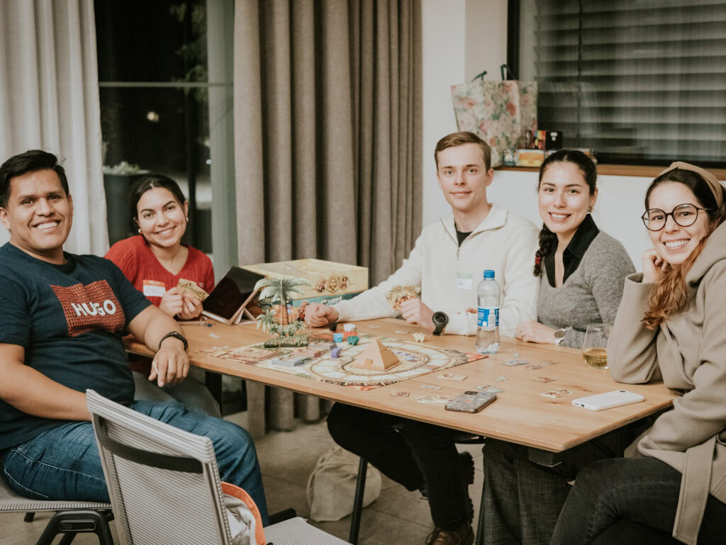 Fünf junge Erwachsene sitzen um einen Holztisch, lachen und unterhalten sich.