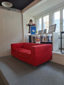 Rotes Sofa vor Fenster mit Büchern und Dekorationen auf dem Regal.