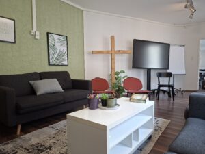 Ein moderner Konferenzraum mit einem schwarzen Sofa, einem weißen Tisch, einem Fernseher, zwei roten.