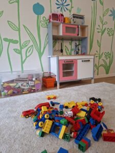 Kinderspielzeugküche mit Lego-Steinen und Spielzeugautos auf Teppich.