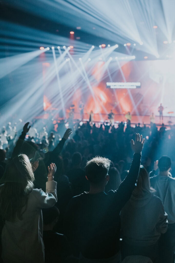 People in front of the stage raise their hands while the lights are directed at the stage.