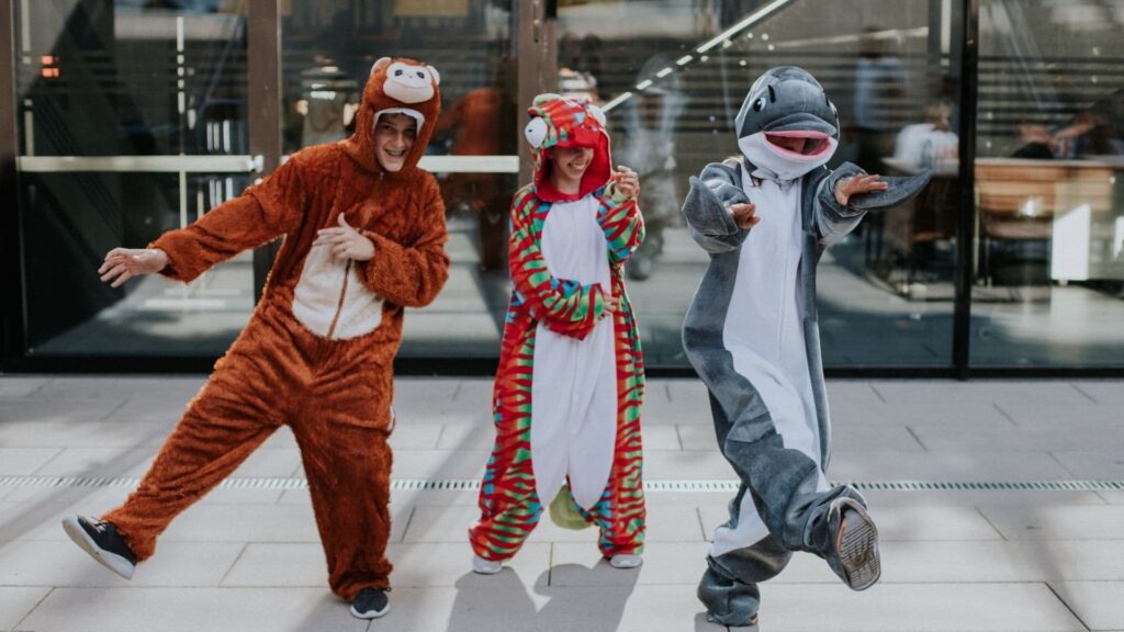 Children dressed in animal costumes laugh and dance outdoors.