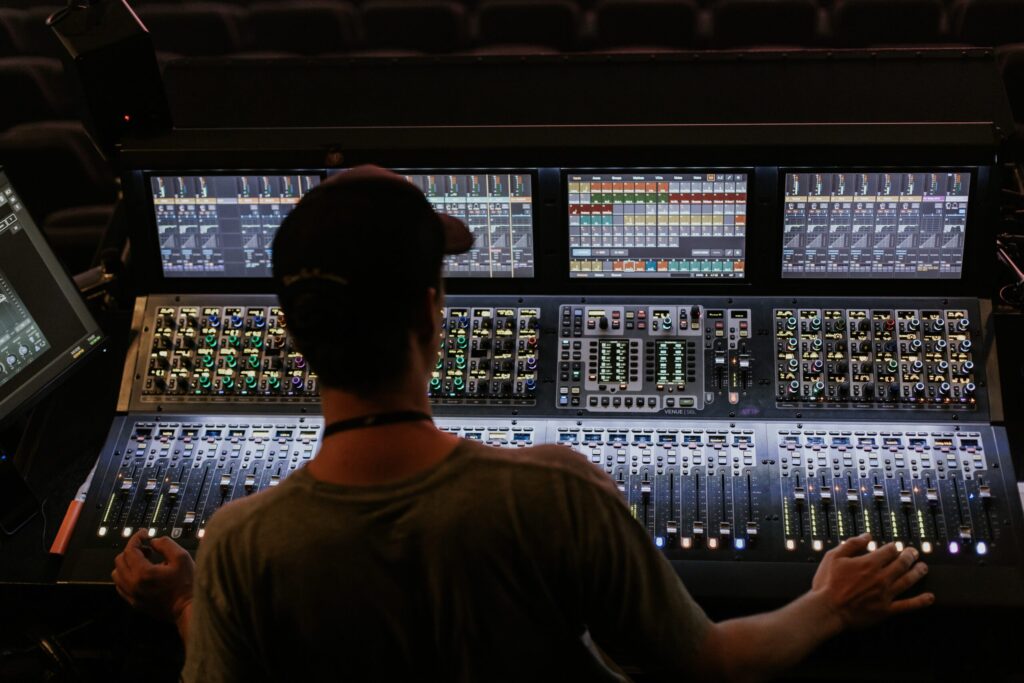 The user controls a large digital mixing console with multiple screens, buttons, and controls.