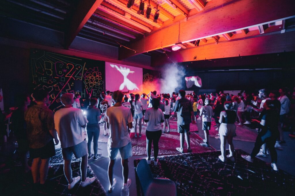 Crowd dancing in a dark room lit by colored lights.