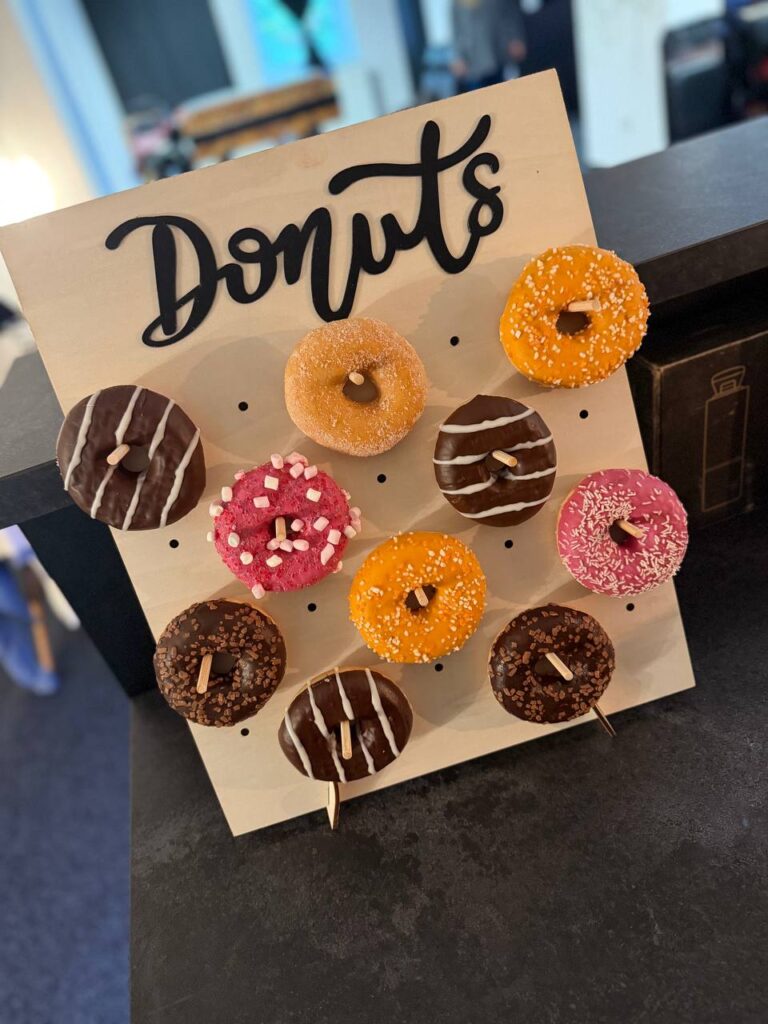 Devět donutit na stojanu s nápisem Donuts, různé polevy a posypy.