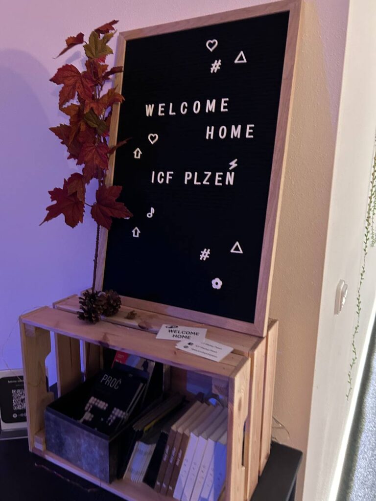 Černá tabule s nápisem Welcome Home ICF Plzen a symboly.