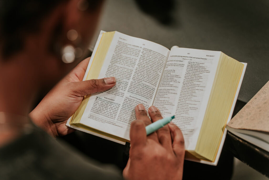 Person liest ein offenes Buch mit Text, hält einen Stift in der Hand.