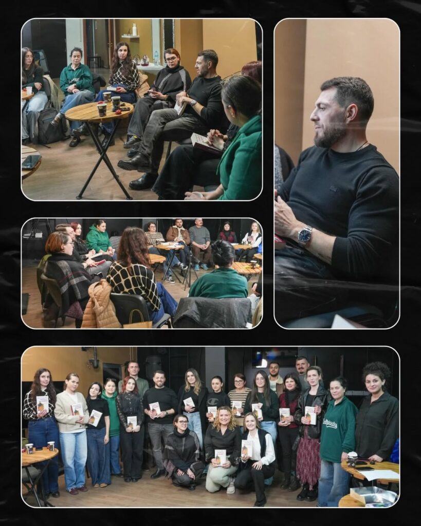 People sitting and standing in a room, some holding books or papers.