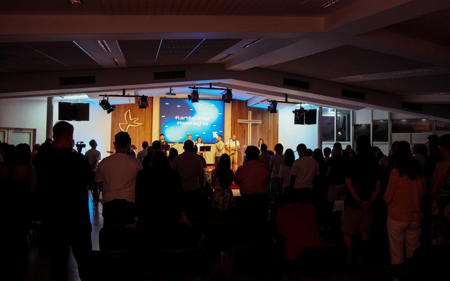 People gathered in a church during a service, facing the altar with a cross and a screen.