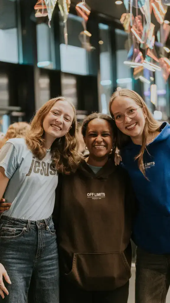 Drei junge Frauen stehen Arm in Arm und lachen.