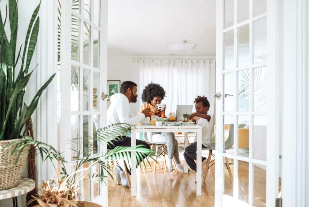 Family sitting at a table in a bright living room, children and adults eating.