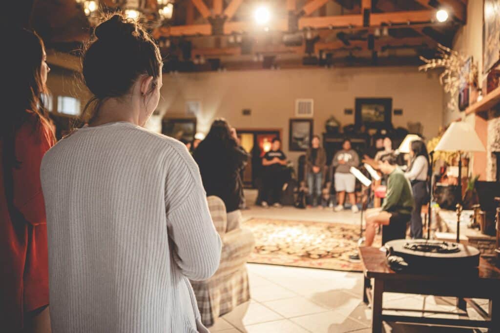 Several people sitting and standing in a room with a wooden ceiling and decorations.