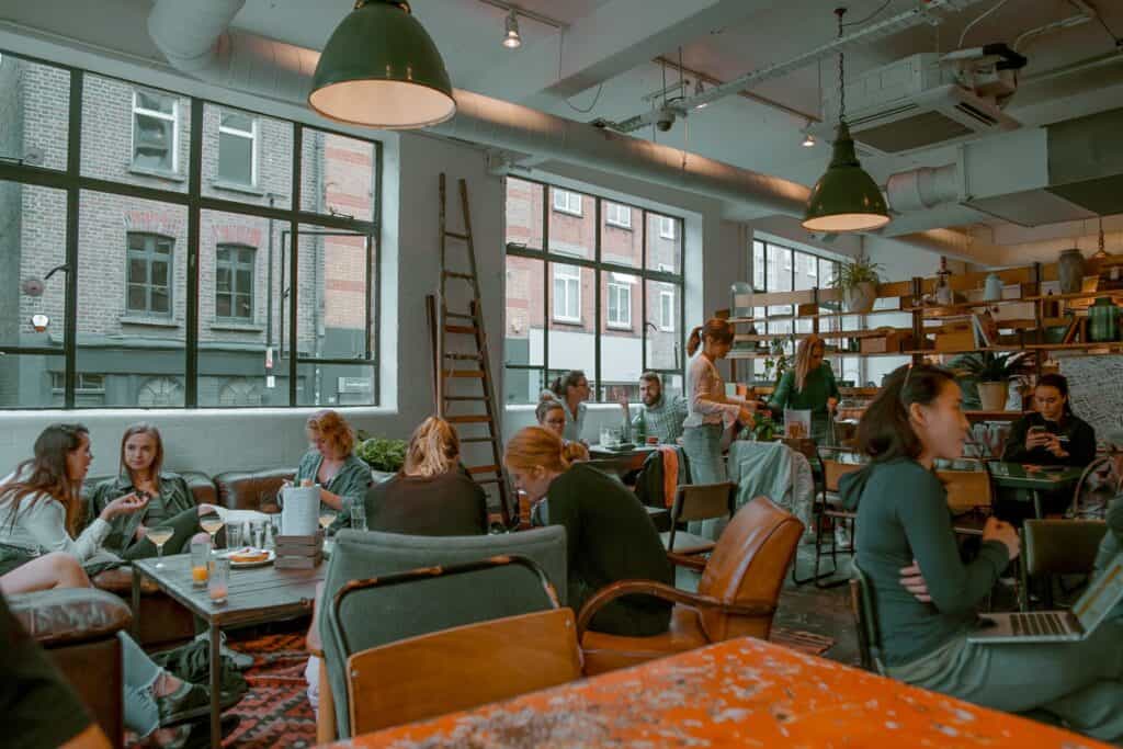 Several people sitting at tables in a bright room with large windows.