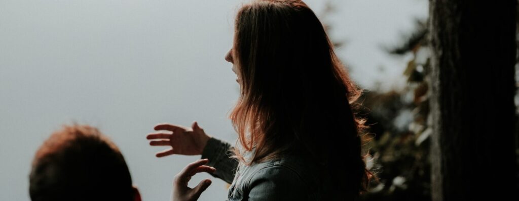 Woman with long hair talking to another person outdoors at sunset.
