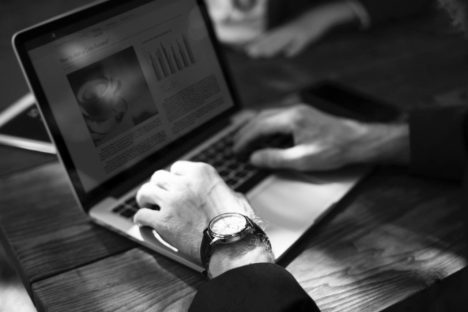 Hand with wristwatch typing on laptop keyboard, screen showing charts.