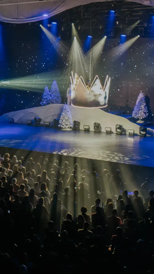Bühne mit Kronen- und Weihnachtsbaum-Dekorationen, bunte Lichter und Schneeflocken.
