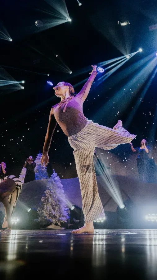 Balletttänzerin auf Bühne in Pose mit ausgestrecktem Arm und Bein.