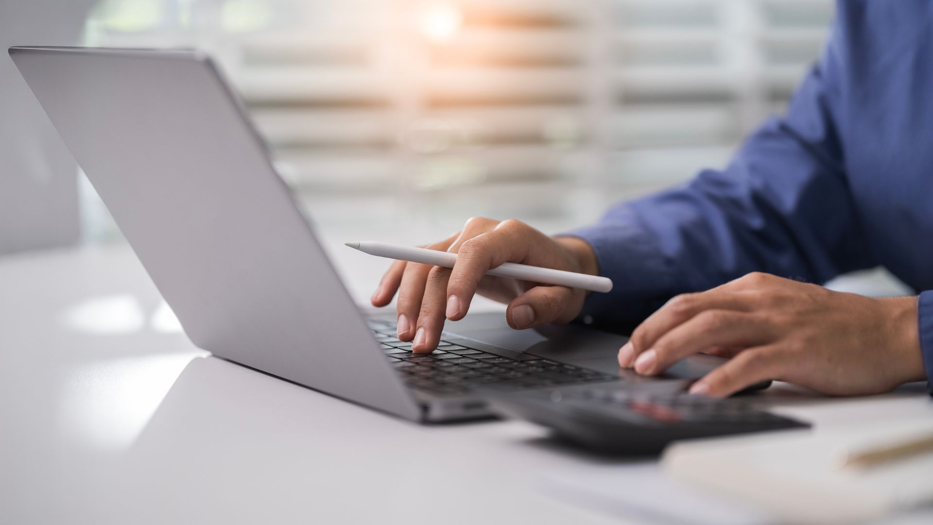 Person tippt auf Laptop mit Stift in der Hand.