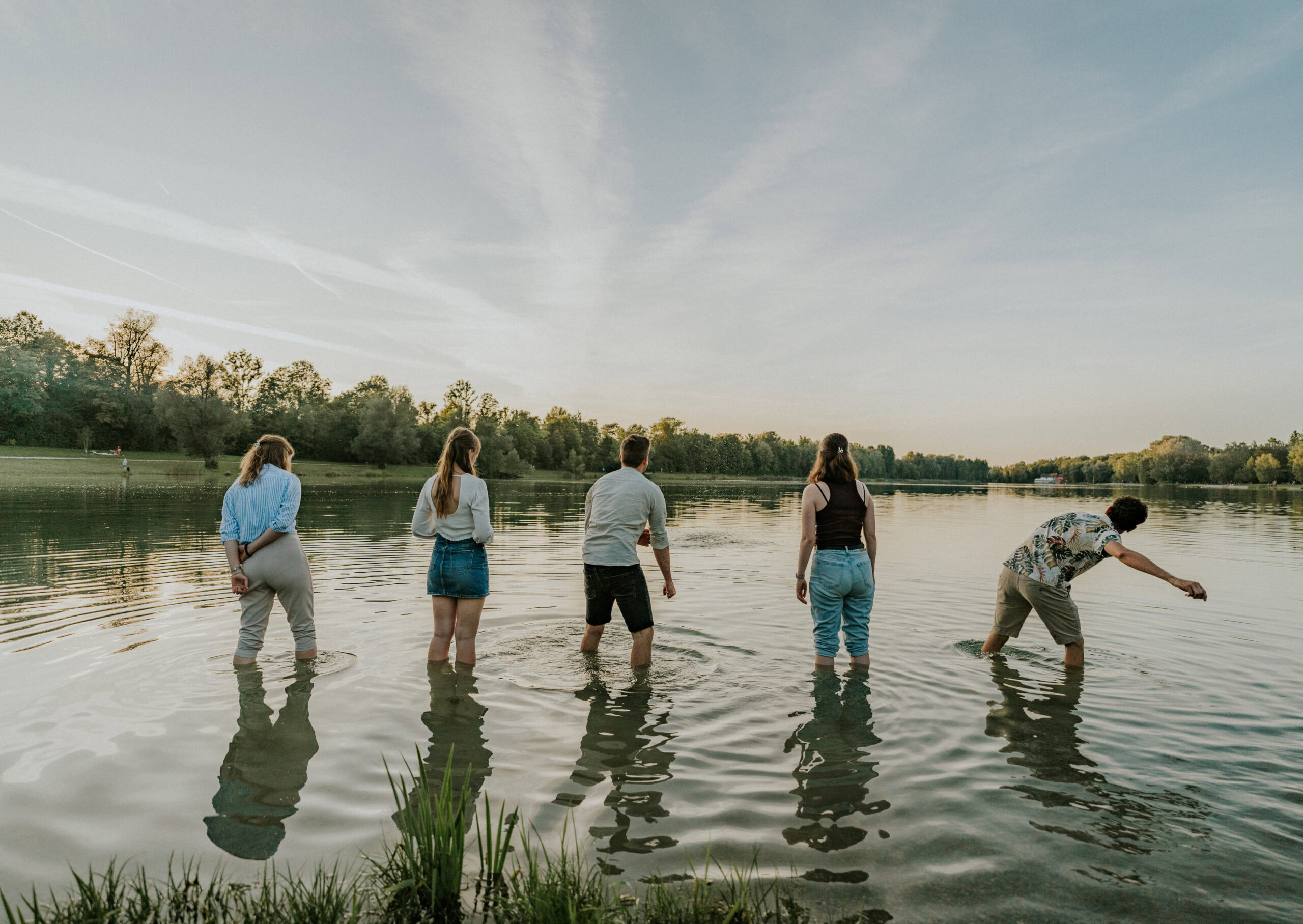 Fünf junge Erwachsene stehen im Wasser eines Sees, einige sind beim Spielen oder Gehen.