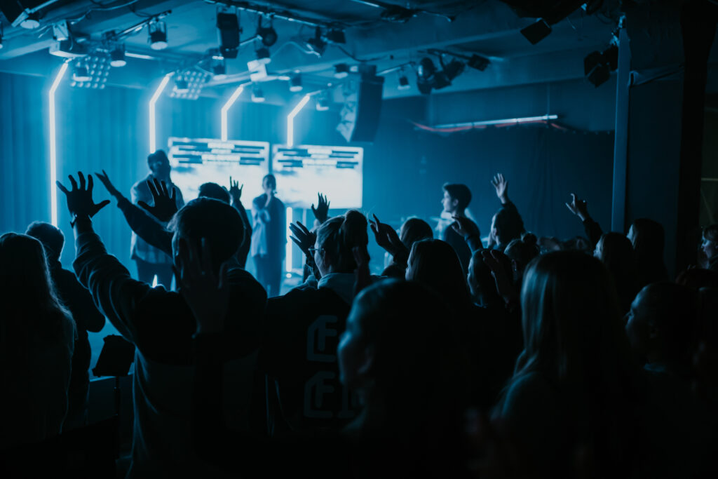 Young people attending a modern church service featuring a light show and music, demonstrating a sense of community and faith in a contemporary church in Berlin.