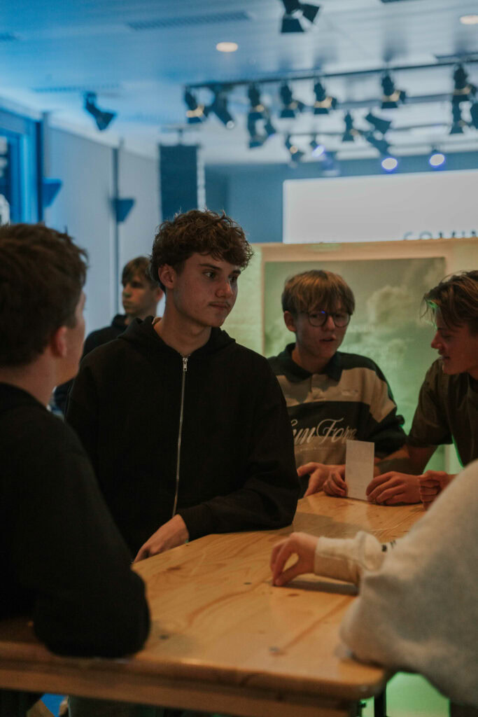 Junge Leute im Gespräch bei einer Veranstaltung in Bern, Schweiz, mit moderner Lichttechnik im Hintergrund.