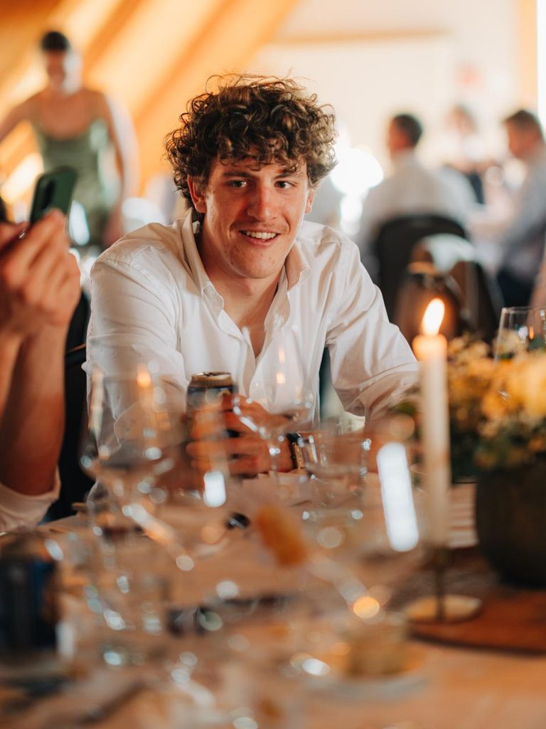 Junger Mann mit lockigem Haar sitzt an einem Tisch bei einem Essen.