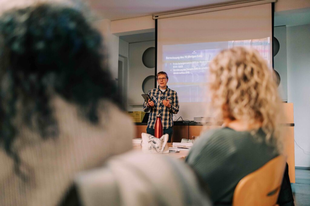 Frau hält eine Präsentation vor einem Publikum im Raum, mit einem Projektor im Hintergrund, der eine PowerPoint-Folie zeigt, bei einer Veranstaltung der ICF Kirche in Hamburg.