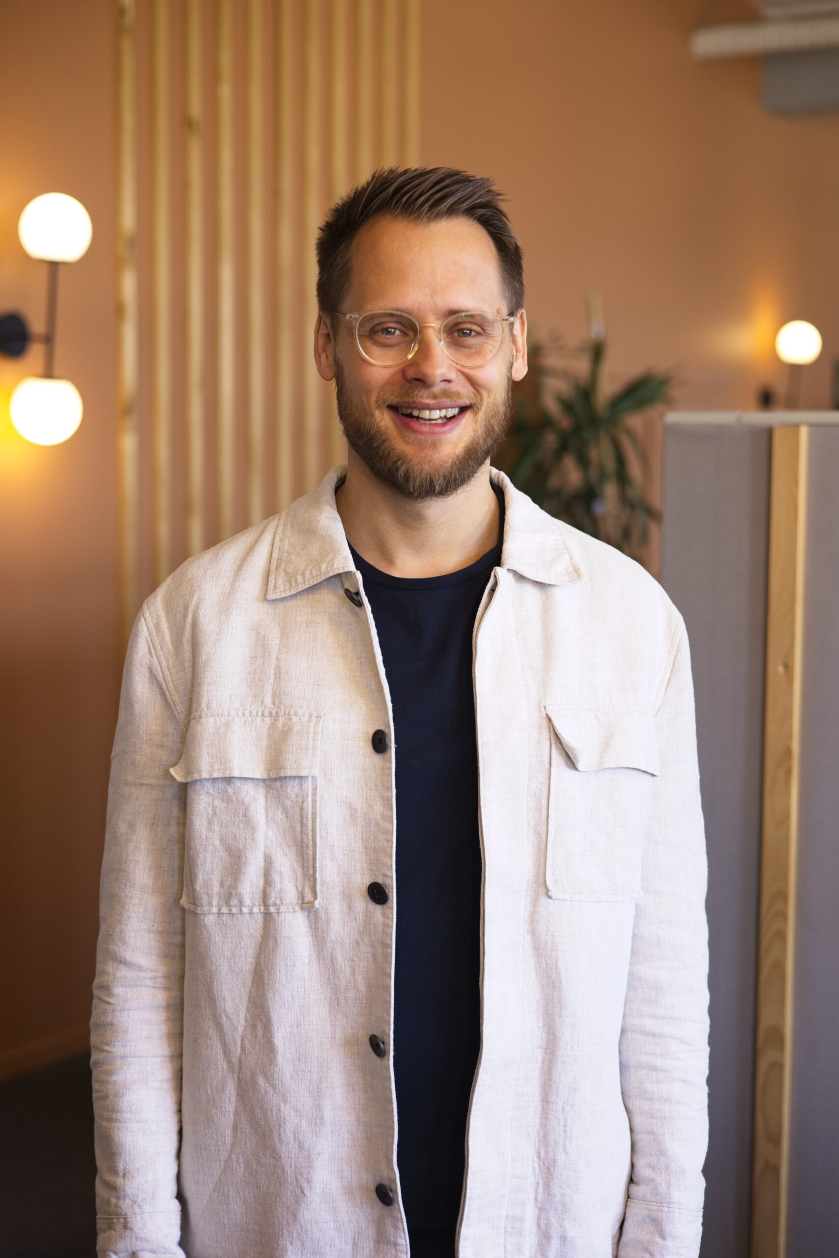 Lächelnder Mann mit Brille und Bart in modernem Raum, repräsentiert die offene Gemeinschaft der ICF Basel Kirche.