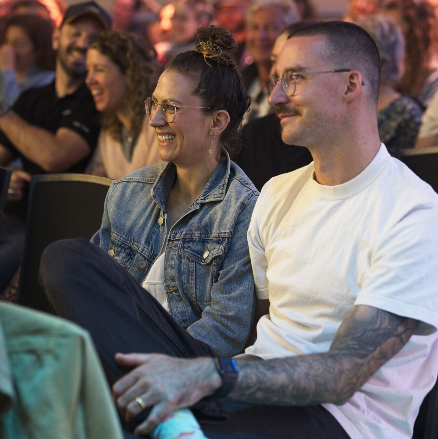 Menschen sitzen in einem Publikum, lachen und schauen nach vorne.
