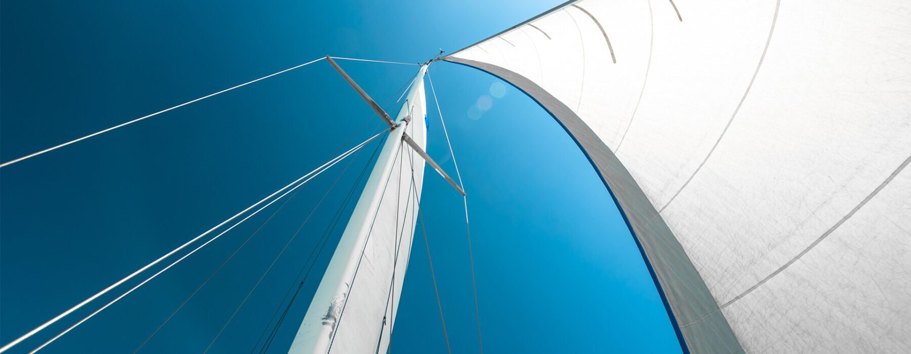 Segelboot mit blauen und weißen Segeln im Sonnenlicht, Symbol für Freiheit und Abenteuer, auf dem Wasser.