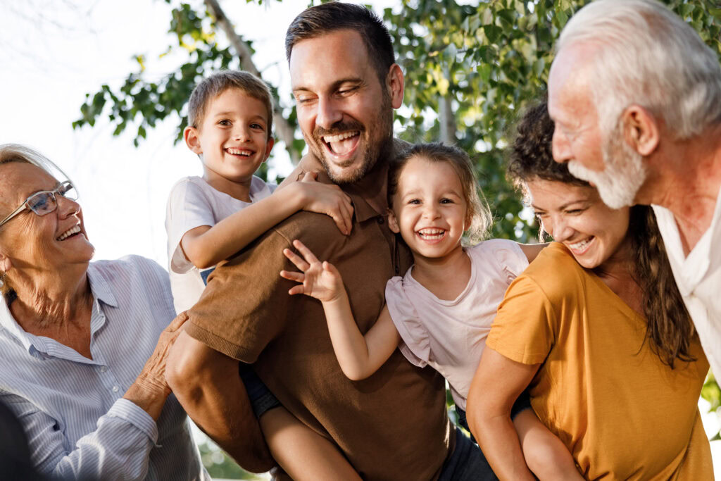 Familie mit Kindern und Großeltern im Park, lachend und umarmend.