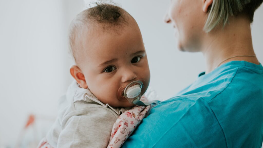 Kleines Baby mit Schnuller auf der Schulter einer Frau.