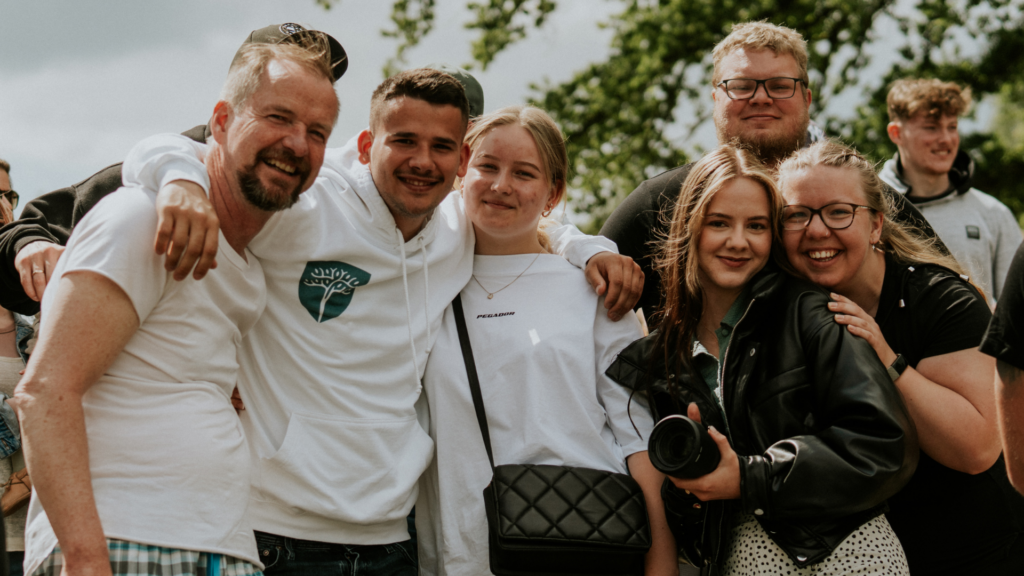 Sechs Menschen stehen im Freien, lachen und umarmen sich.