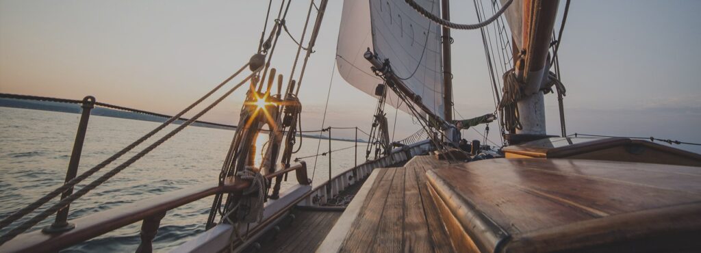 Blick vom Deck eines Segelschiffs auf die Segel und das Wasser.